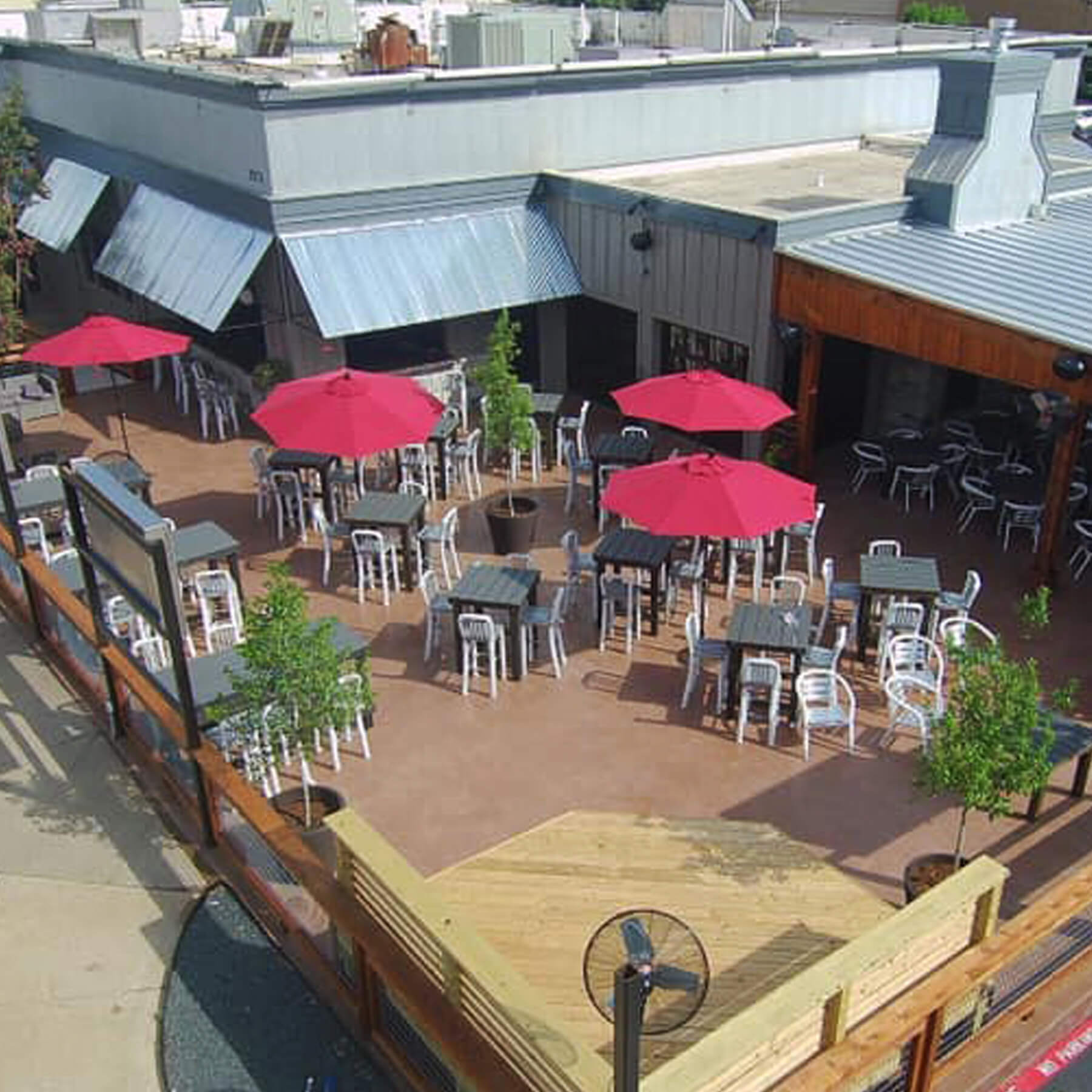 A patio with tables and chairs, umbrellas and trees.
